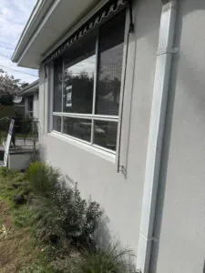 Side wall finished with fine-textured light grey render and a white downpipe in Keysborough.